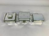 three small silver boxes sitting on top of a white surface