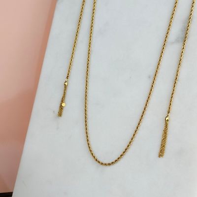 un collier à chaîne en or orné d'un pompon, posé sur une dalle de marbre