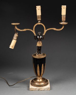 une lampe de table noire et dorée sur laquelle sont posées trois bougies