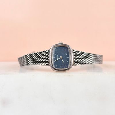 un gros plan d'une montre posée sur une table, sur fond rose