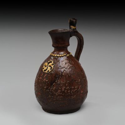 un vieux vase marron orné d'un motif doré sur l'anse