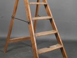 Un vieil escabeau en bois est appuyé contre un mur gris.