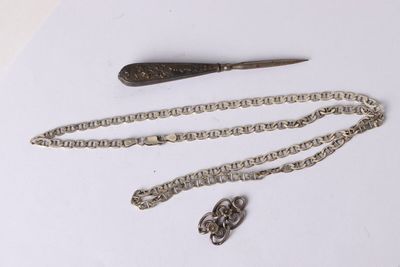 une chaîne en argent et un couteau posés sur une surface blanche