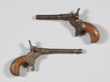 une paire de revolvers anciens en laiton avec des crosses en bois, posés sur une surface blanche