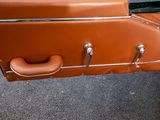 a brown suitcase sitting on the ground next to a car