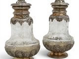 une paire de vases en argent et en verre posés sur des socles, disposés sur une surface blanche