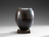 un vase noir posé sur un socle en bois, sur une surface blanche