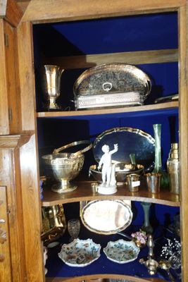 une armoire d'angle sur laquelle sont disposés de nombreux objets en argent