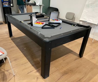 une table de billard au milieu d'une pièce, sur laquelle est posé un ordinateur portable