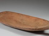 un vieux bol en bois muni d'une poignée, posé sur une surface blanche
