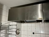 une hotte en acier inoxydable dans une cuisine où une casserole et une poêle sont suspendues au plafond