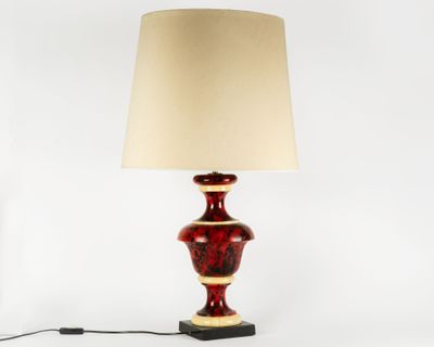 a red table lamp with a beige shade on top of it