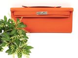 an orange purse next to a green plant on a white surface