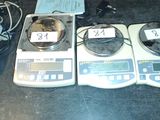 trois balances électroniques posées sur une table, sur lesquelles sont apposées des étiquettes