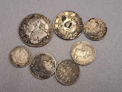 six types différents de pièces d'argent sur une surface grise