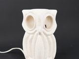 a white ceramic owl lamp with a white cord on a black background