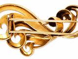 an image of a gold colored brooch with swirls on it