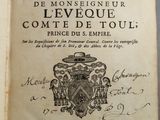 un livre ouvert sur lequel figure l'image d'un blason et un blason
