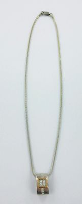 collier en argent et en or avec un pendentif de forme carrée sur fond blanc