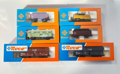 six wagons de train miniature dans leurs boîtes, posés sur une surface blanche
