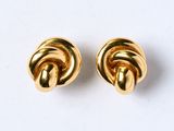 une paire de boucles d'oreilles en forme de nœud, de couleur dorée, posées sur un fond blanc