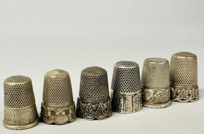 six antique thimbles lined up in a row on a white surface