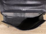 black leather handbag on wooden table with white wall in background
