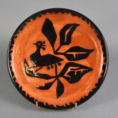 an orange and black plate with a bird on it on a stand