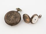 two antique pocket watches are sitting next to each other on a white surface