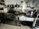 a kitchen with a stove, oven, sink, and shelves