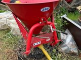 un homme à la brouette rouge assis dans l'herbe à côté d'un tas de vieilleries
