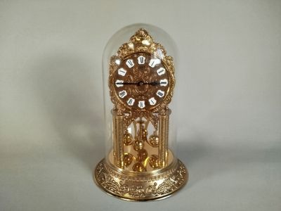 une horloge en or posée sur une table, sous un dôme en verre