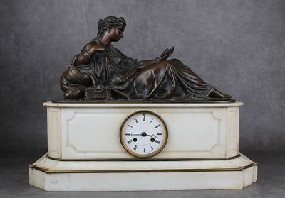une statue représentant une femme assise sur un socle de marbre, avec une horloge devant elle