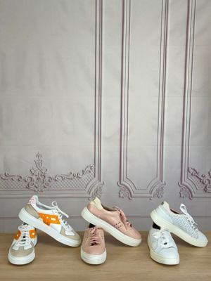 five pairs of white and pink sneakers lined up on a wooden table