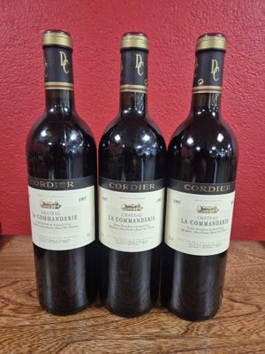 three bottles of wine sit on a wooden table in front of a red wall