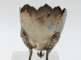 a silver vase that has a bird on it ' s legs