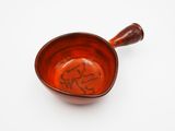 a small red bowl with a wooden handle on a white surface