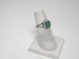 un gros plan d'une bague sertie d'une pierre verte, posée sur un socle