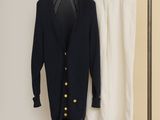 Deux pantalons blancs et un cardigan noir sont suspendus à un portant.