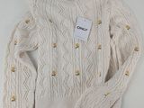 Le pull est blanc et comporte des boutons.