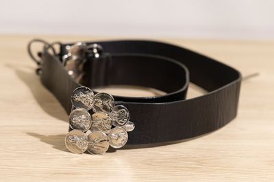 ceinture en cuir noir avec une boucle en forme de fleur en métal argenté posée sur une surface en bois