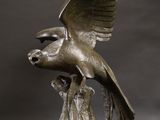 bronze sculpture of a bird on a branch with its wings spread