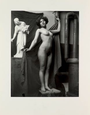 black and white photograph of a naked woman standing on a pedestal