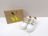 une paire de chaussures blanches avec des lanières dorées, posée à côté d'une boîte en carton
