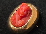 une image représentant une broche rouge et dorée avec le visage d'un homme