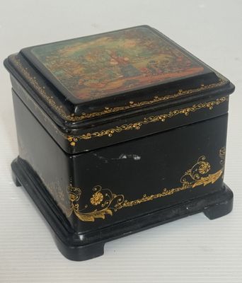 boîte décorée de noir et d'or, posée sur un socle, sur fond blanc