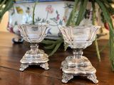deux bougeoirs en verre posés sur une table, avec des fleurs en arrière-plan