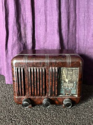 an old radio sitting on the floor next to a purple curtain