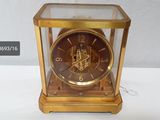 a gold clock with a glass case on a white table