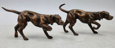 deux figurines en bronze représentant des chiens en train de courir sur une surface blanche